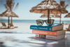 Strand mit Strohsonnenschirmen und Bücher und Sonnenbrille im Vordergrund